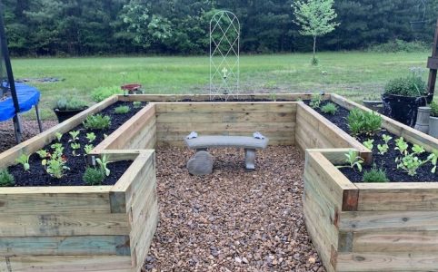 Layers at the bottom of a raised garden bed including cardboard, gravel, sticks, and soil for proper drainage and healthy plant growth