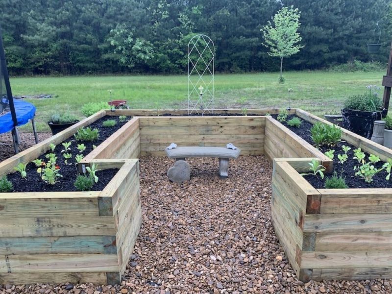 Layers at the bottom of a raised garden bed including cardboard, gravel, sticks, and soil for proper drainage and healthy plant growth