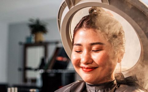 A person relaxing with a Japanese scalp steaming machine emitting a gentle mist over their hair in a spa