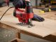 Corded jigsaw making precise curved cut in plywood with clear dust blower active