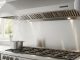 Stainless steel range hood mounted above gas cooktop showing proper sizing that extends beyond cooktop width for effective ventilation