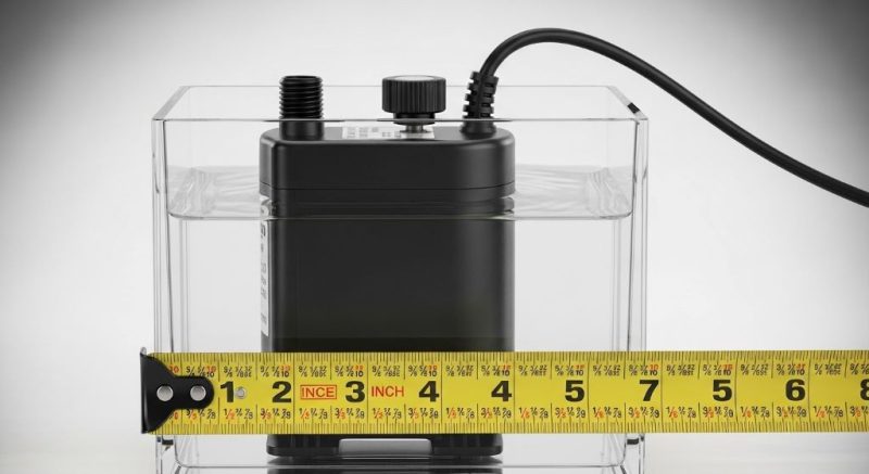 Small submersible fountain pump with adjustable flow control sitting in clear water next to measuring tape showing size comparison