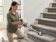 A person using a lightweight cordless handheld vacuum to clean a carpeted staircase in a bright modern home, demonstrating easy carpet stair cleaning technique