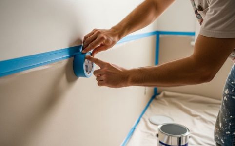 A person carefully pressing painter's tape along a wall edge before painting to achieve clean paint lines