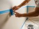 A person carefully pressing painter's tape along a wall edge before painting to achieve clean paint lines