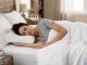 A person sleeping on a contoured ergonomic pillow with proper neck and spine alignment on a white bed