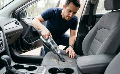 A man using a lightweight cordless handheld vacuum to clean a gray fabric car seat interior