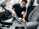 A man using a lightweight cordless handheld vacuum to clean a gray fabric car seat interior